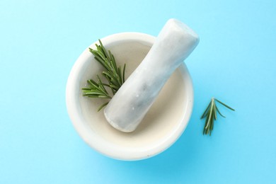 Photo of Ceramic mortar with rosemary and pestle on light blue background, top view