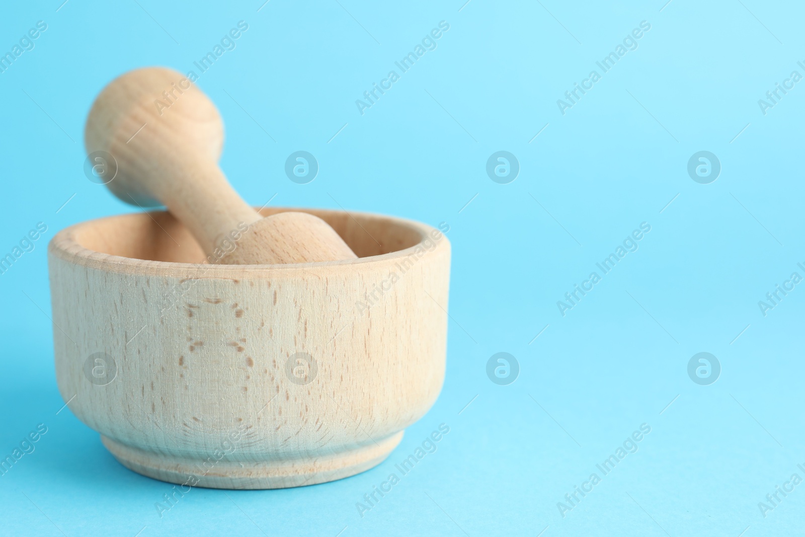 Wooden mortar and pestle on light blue background, closeup. Space for text Photo of Wooden mortar and pestle on light blue background, closeup. Space for text
