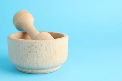 Photo of Wooden mortar and pestle on light blue background, closeup. Space for text