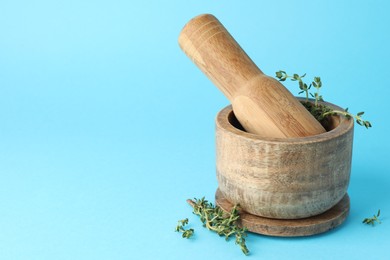 Photo of Wooden mortar with thyme and pestle on light blue background, closeup. Space for text