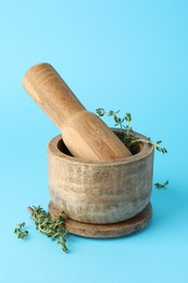 Photo of Wooden mortar with thyme and pestle on light blue background, closeup