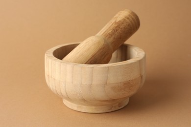 Photo of Wooden mortar and pestle on light brown background, closeup