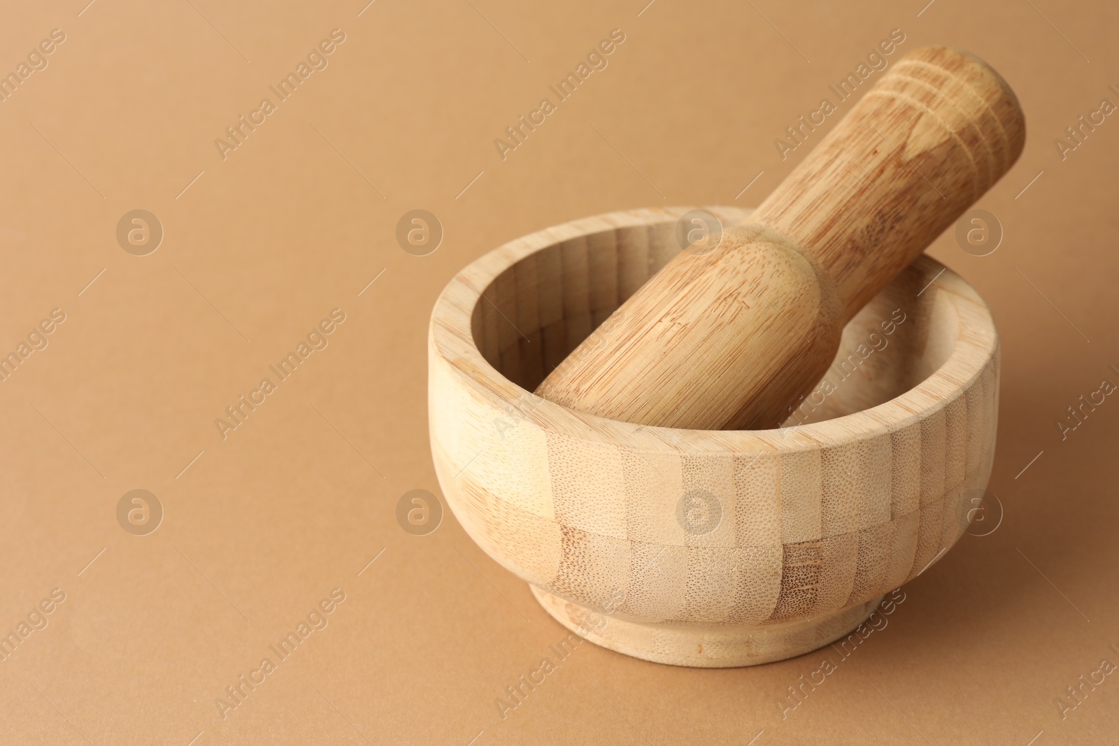 Wooden mortar and pestle on light brown background, closeup. Space for text Photo of Wooden mortar and pestle on light brown background, closeup. Space for text