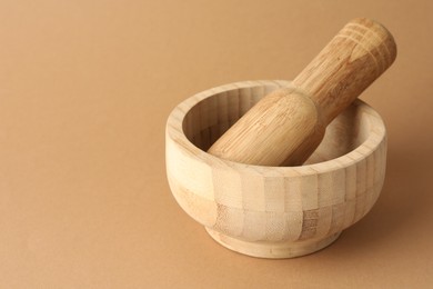 Photo of Wooden mortar and pestle on light brown background, closeup. Space for text
