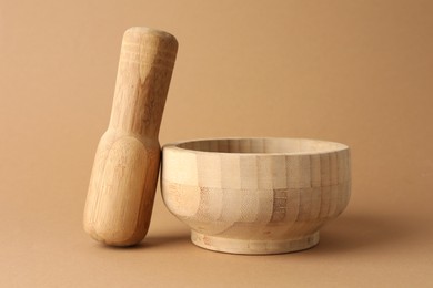 Photo of Wooden mortar and pestle on light brown background, closeup