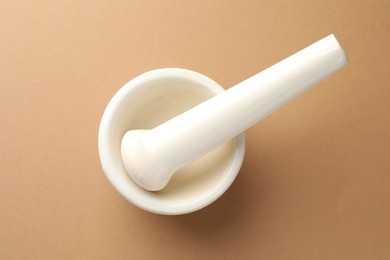 Photo of Ceramic mortar and pestle on light brown background, top view