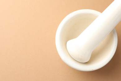 Photo of Ceramic mortar and pestle on light brown background, top view. Space for text