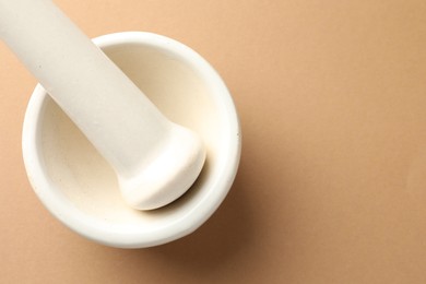 Photo of Ceramic mortar and pestle on light brown background, top view. Space for text
