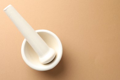 Photo of Ceramic mortar and pestle on light brown background, top view. Space for text