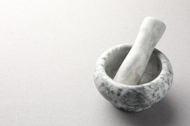 Photo of Marble mortar and pestle on light grey background, closeup. Space for text