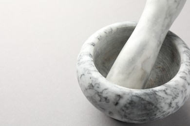 Photo of Marble mortar and pestle on light grey background, closeup. Space for text