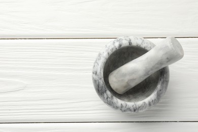 Photo of Marble mortar and pestle on white wooden table, top view. Space for text