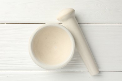 Photo of Ceramic mortar and pestle on white wooden table, top view