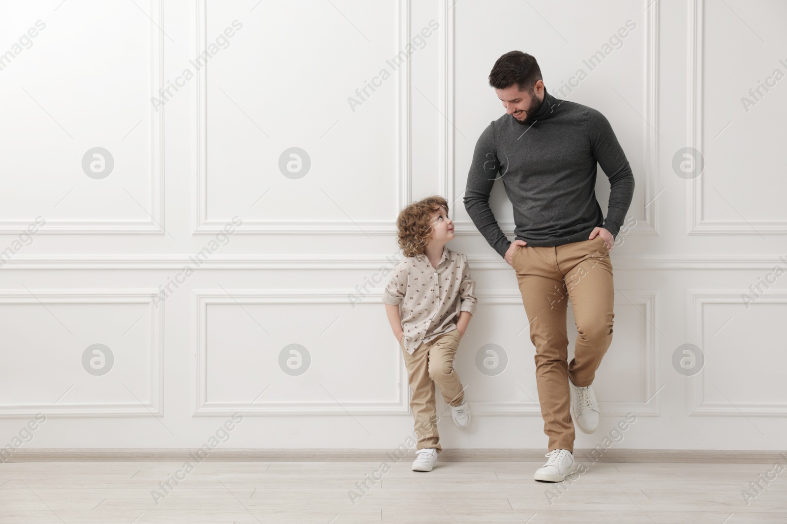 Photo of Happy father and his son near white wall indoors, space for text