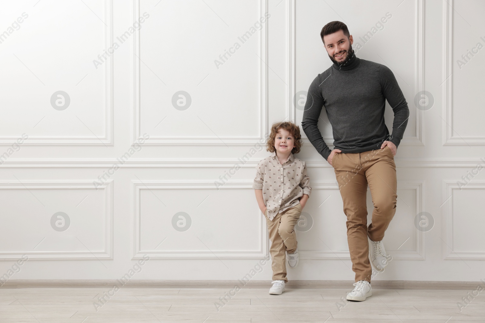 Photo of Happy father and his son near white wall indoors, space for text