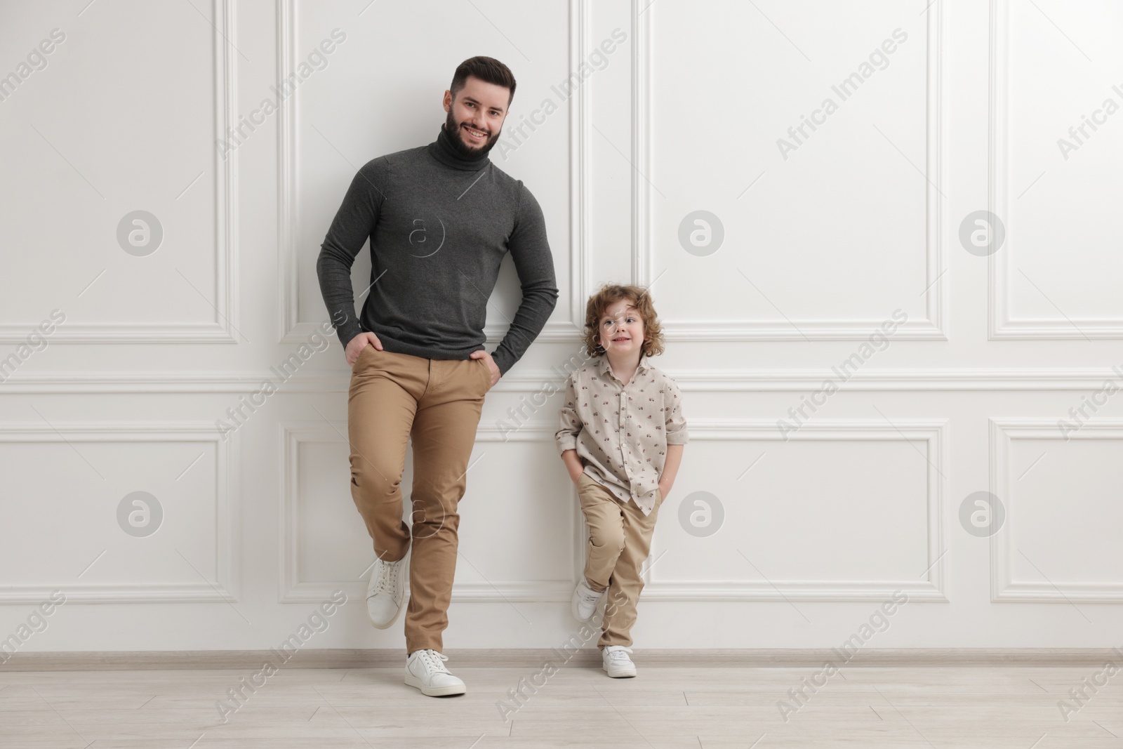 Happy father and his son near white wall indoors Photo of Happy father and his son near white wall indoors