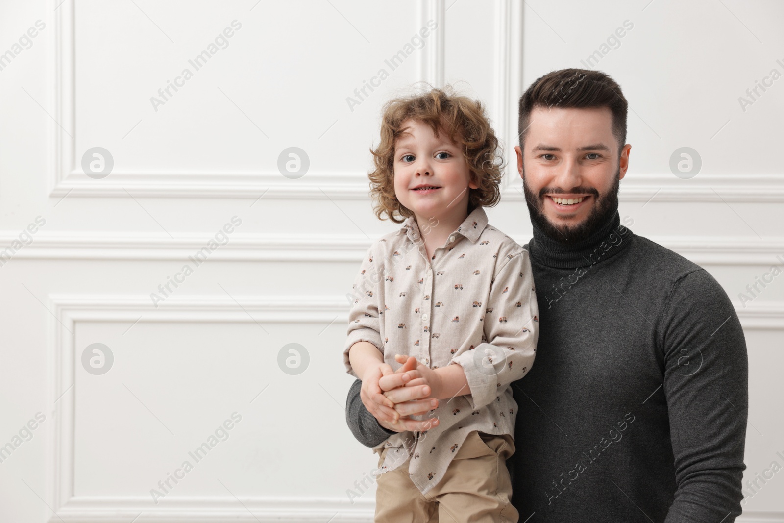 Happy father and his son near white wall indoors, space for text Photo of Happy father and his son near white wall indoors, space for text