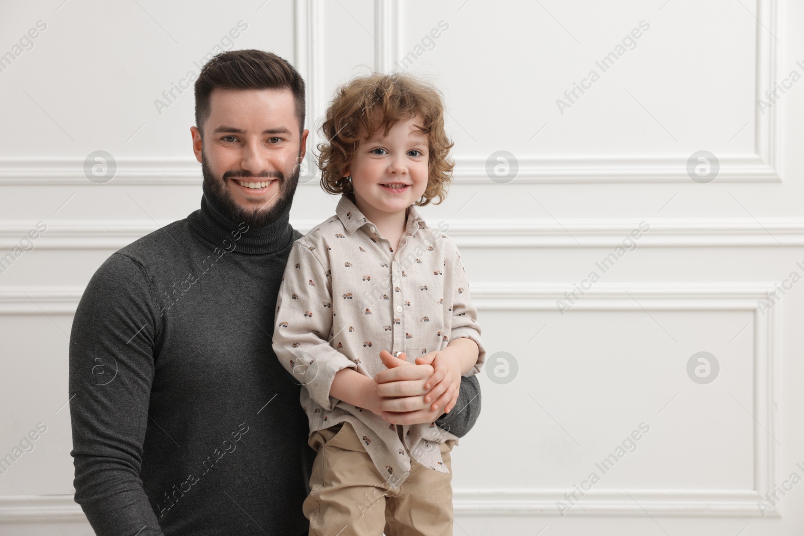 Photo of Happy father and his son near white wall indoors, space for text