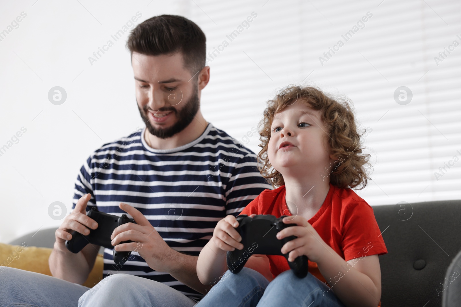 Happy father and his son playing with game controllers together on sofa at home Photo of Happy father and his son playing with game controllers together on sofa at home