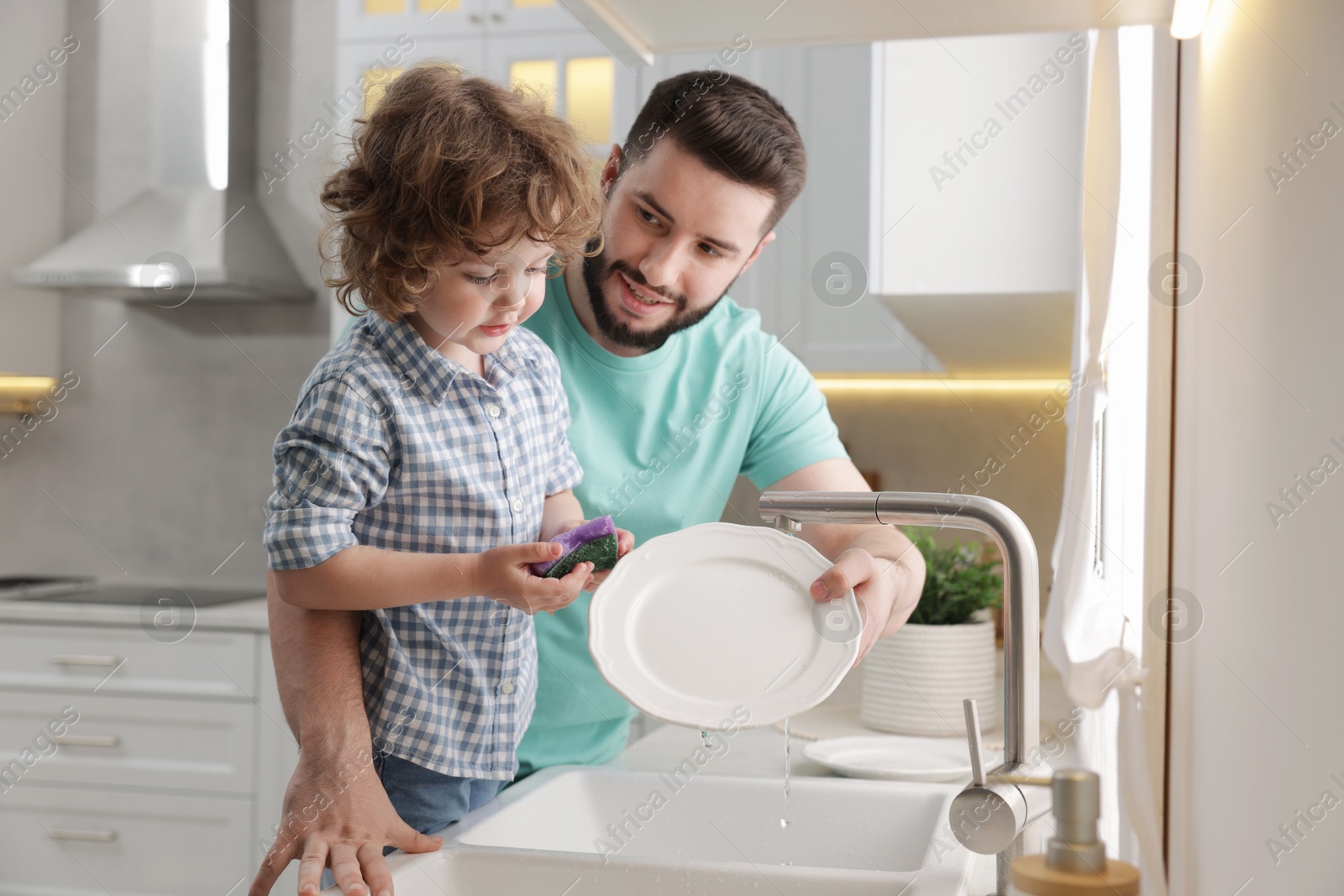 Father and his son washing dishes together in kitchen at home Photo of Father and his son washing dishes together in kitchen at home