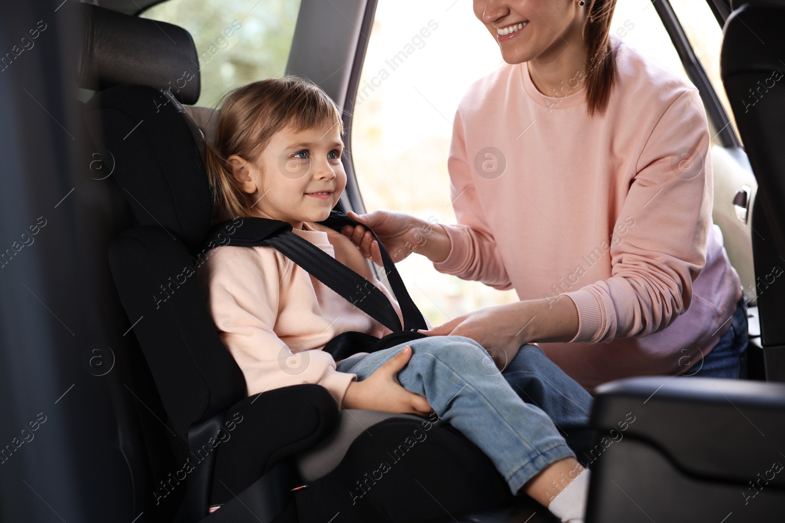 Mother fastening her daughter in child safety seat inside car, closeup Photo of Mother fastening her daughter in child safety seat inside car, closeup