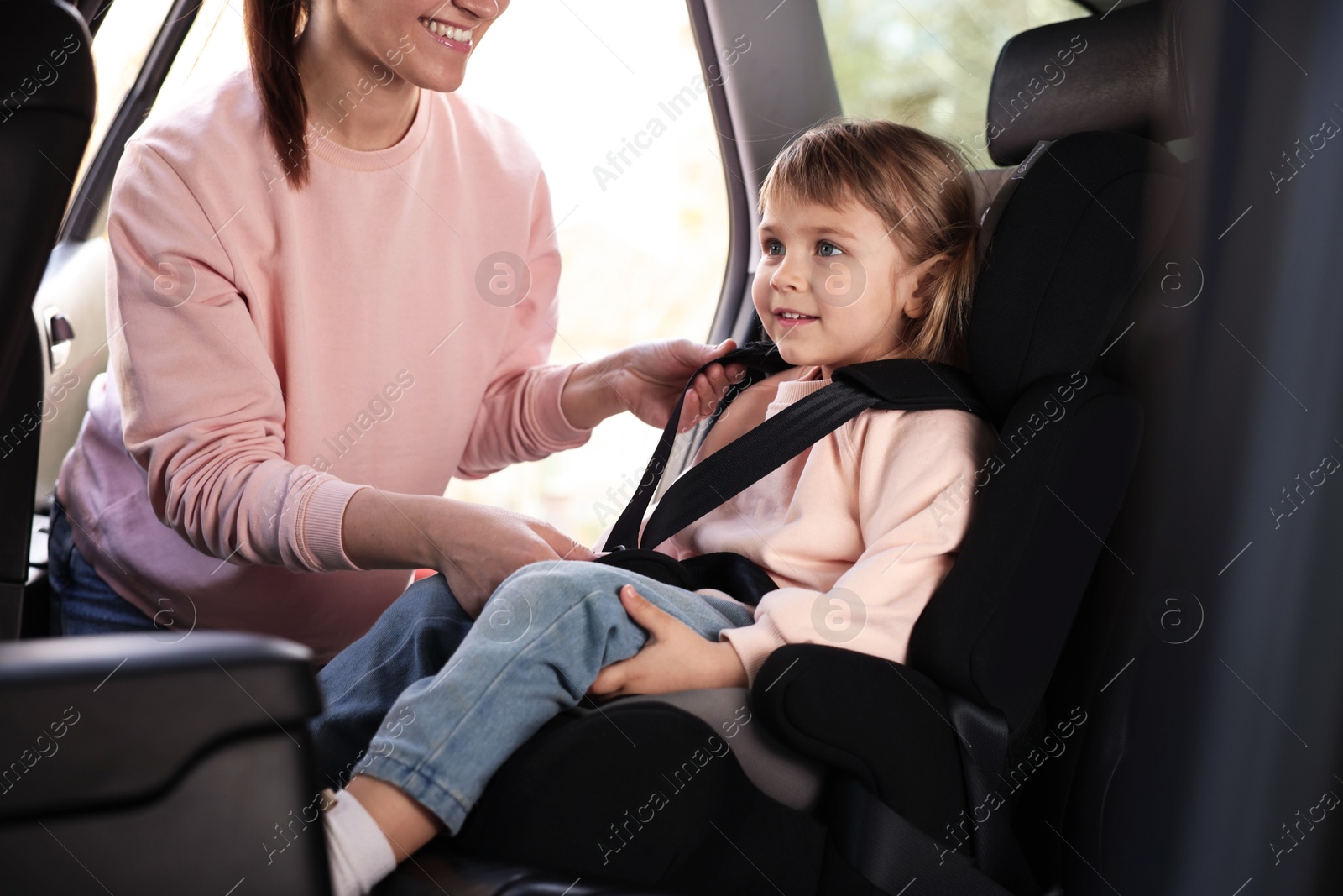 Mother fastening her daughter in child safety seat inside car, closeup Photo of Mother fastening her daughter in child safety seat inside car, closeup