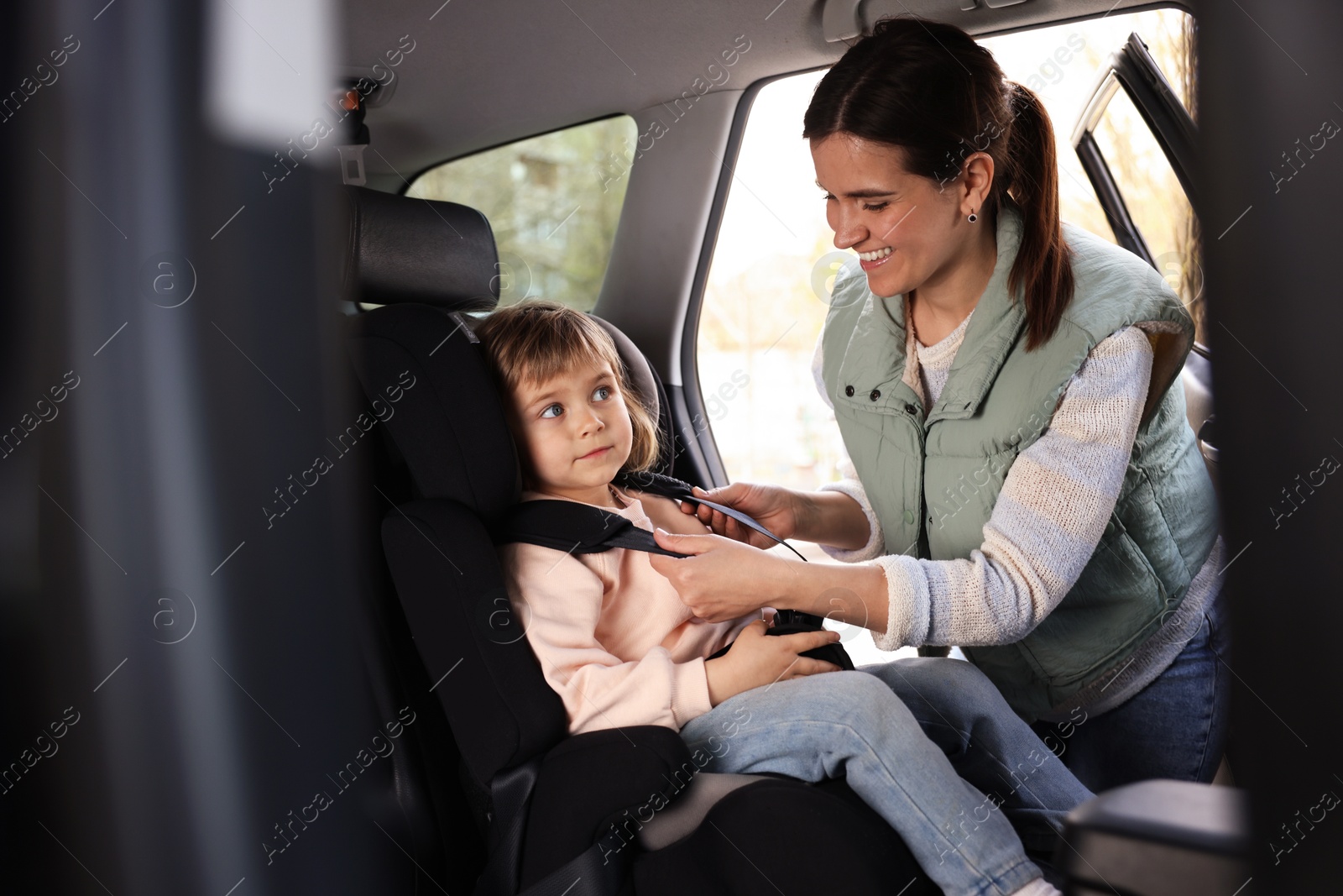 Photo of Happy mother fastening her daughter in child safety seat inside car