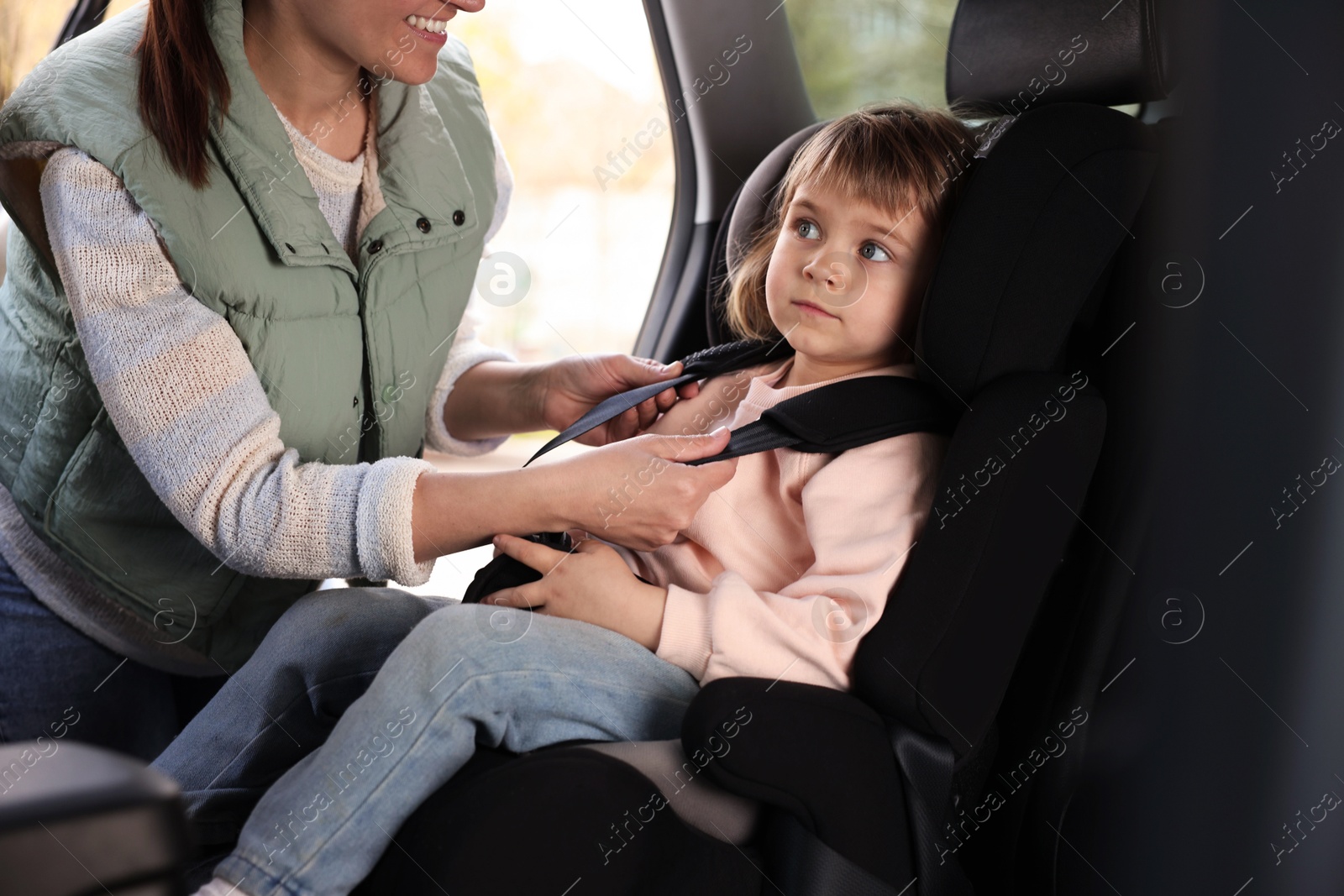 Photo of Mother fastening her daughter in child safety seat inside car, closeup