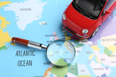Photo of Road trip concept. Toy car and magnifying glass on world map, above view