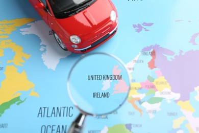 Photo of Road trip concept. Toy car and magnifying glass on world map, above view