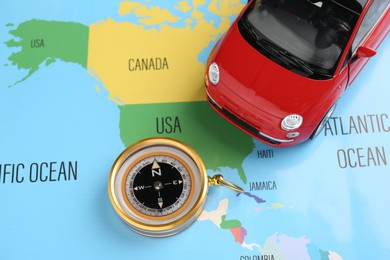 Photo of Road trip concept. Toy car and compass on world map, above view