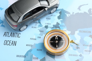 Photo of Road trip concept. Toy car and compass on world map, above view