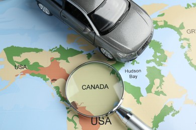 Photo of Road trip concept. Toy car and magnifying glass on world map, above view