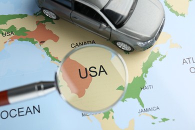 Photo of Road trip concept. Toy car and magnifying glass on world map, above view