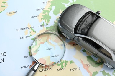 Photo of Road trip concept. Toy car and magnifying glass on world map, above view