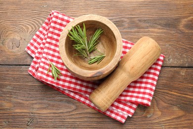 Photo of Mortar with rosemary, pestle and cloth on wooden table, flat lay