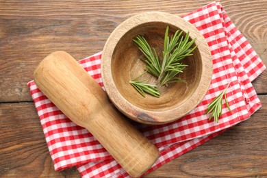 Photo of Mortar with rosemary, pestle and cloth on wooden table, flat lay
