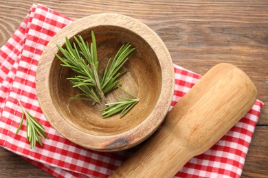 Photo of Mortar with rosemary, pestle and cloth on wooden table, flat lay