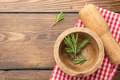 Photo of Mortar with rosemary, pestle and cloth on wooden table, flat lay. Space for text