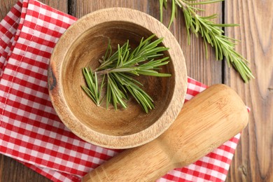 Photo of Mortar with rosemary, pestle and cloth on wooden table, flat lay