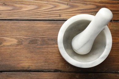 Photo of Marble mortar and pestle on wooden table, top view. Space for text