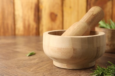 Photo of Mortar with rosemary and pestle on wooden table, closeup. Space for text
