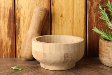 Photo of Mortar with rosemary and pestle on wooden table, closeup