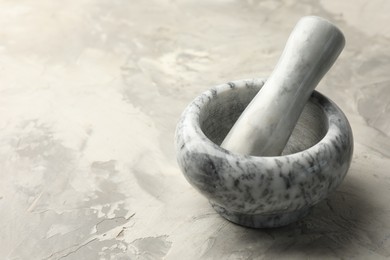 Photo of Marble mortar and pestle on grey textured table, closeup. Space for text