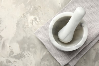 Photo of Marble mortar, pestle and cloth on grey textured table, top view. Space for text