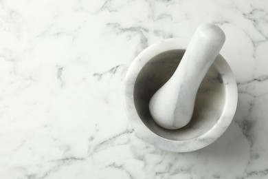 Photo of Mortar and pestle on white marble table, top view. Space for text