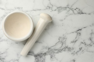 Photo of Ceramic mortar and pestle on white marble table, top view. Space for text