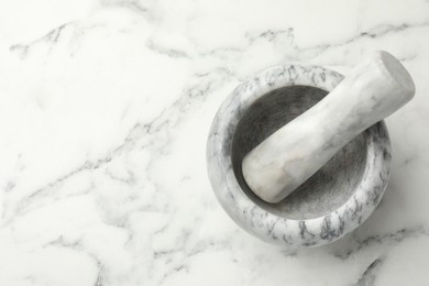 Photo of Mortar and pestle on white marble table, top view. Space for text