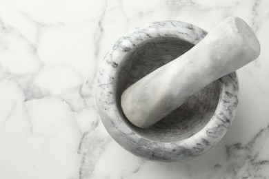 Photo of Mortar and pestle on white marble table, top view. Space for text