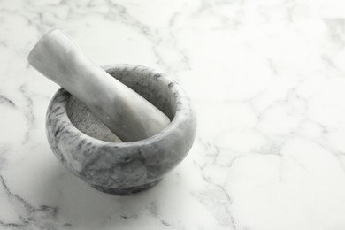 Photo of Mortar and pestle on white marble table, closeup. Space for text